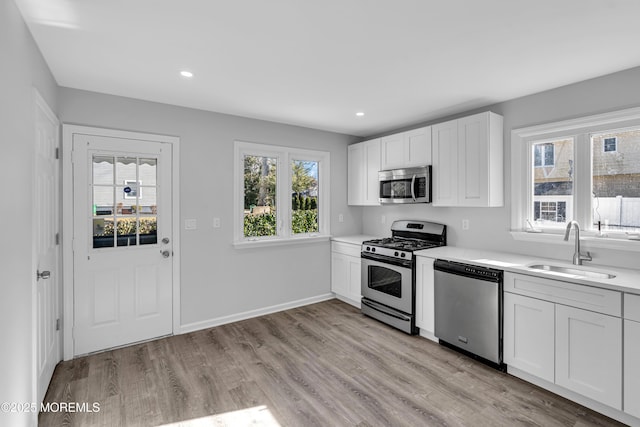 kitchen with appliances with stainless steel finishes, sink, white cabinets, and light wood-type flooring