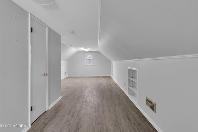 additional living space featuring lofted ceiling, hardwood / wood-style floors, and built in shelves