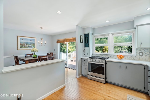 kitchen featuring light wood finished floors, decorative backsplash, light countertops, gray cabinets, and gas stove