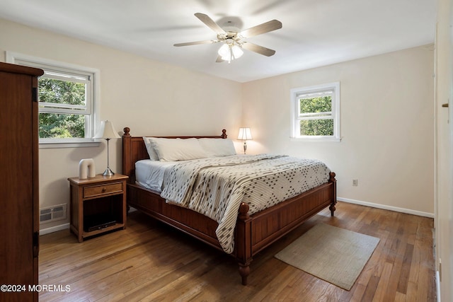 bedroom featuring hardwood / wood-style floors, multiple windows, visible vents, and baseboards