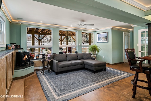 living room featuring baseboards, ceiling fan, ornamental molding, a wood stove, and concrete floors