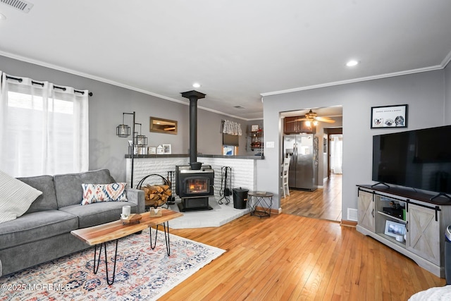 living room with hardwood / wood-style floors, crown molding, ceiling fan, and a wood stove