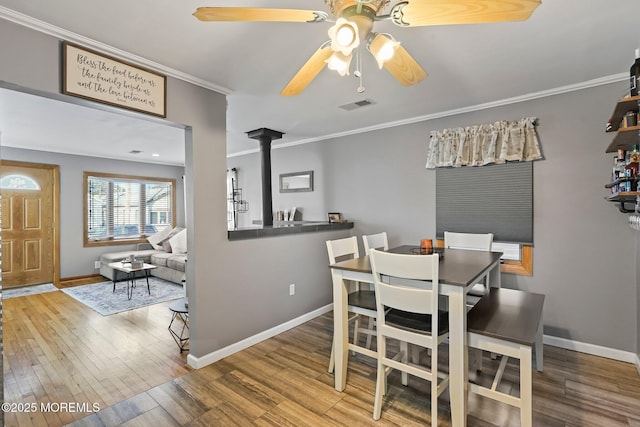 dining room with ceiling fan, ornamental molding, wood-type flooring, and a wood stove