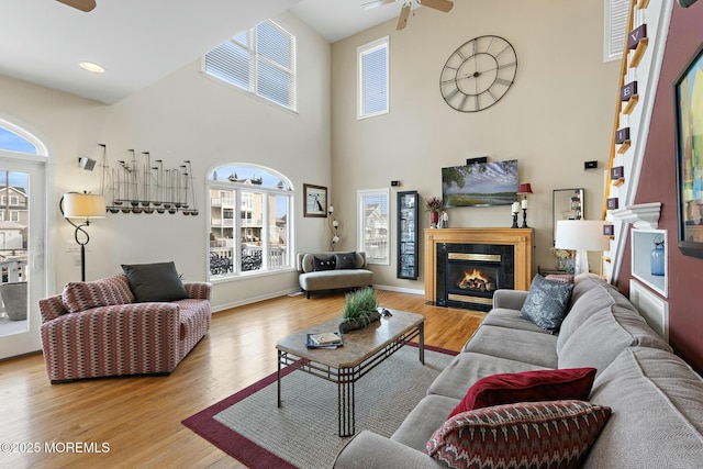 living room with ceiling fan, a premium fireplace, light hardwood / wood-style floors, and a towering ceiling