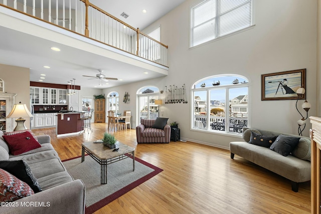 living room featuring sink, a towering ceiling, light hardwood / wood-style floors, and ceiling fan