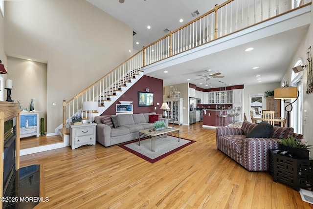 living room with ceiling fan, a towering ceiling, and light hardwood / wood-style flooring