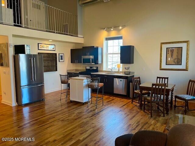 kitchen with appliances with stainless steel finishes, a breakfast bar area, dark wood finished floors, and a towering ceiling