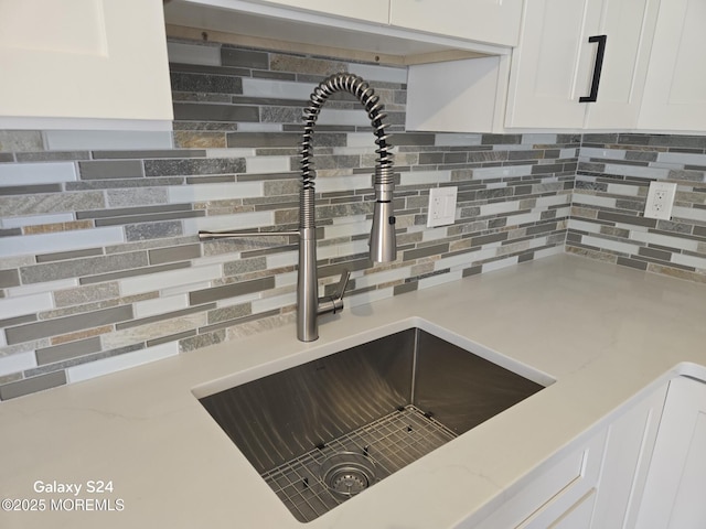 room details featuring tasteful backsplash, light stone countertops, sink, and white cabinets