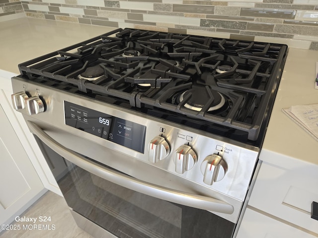 interior details featuring backsplash, stainless steel range with gas stovetop, and white cabinets