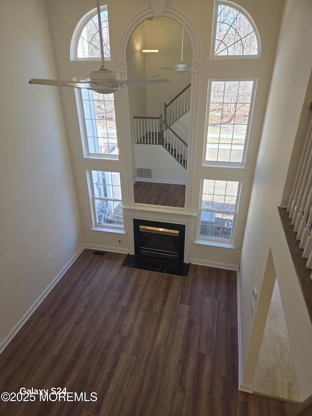 unfurnished living room with ceiling fan, a towering ceiling, and dark hardwood / wood-style flooring