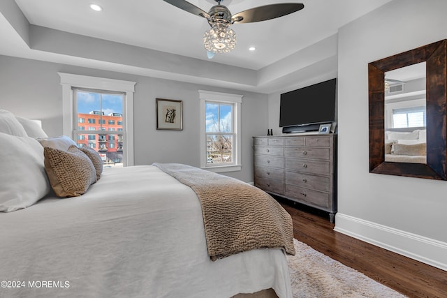 bedroom with dark hardwood / wood-style flooring, a raised ceiling, and ceiling fan