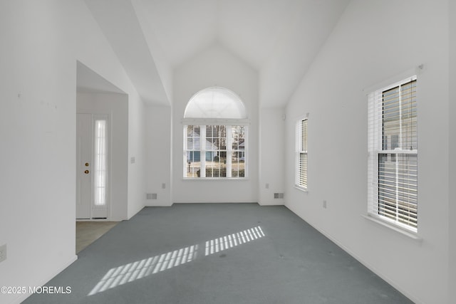 unfurnished living room with high vaulted ceiling and carpet