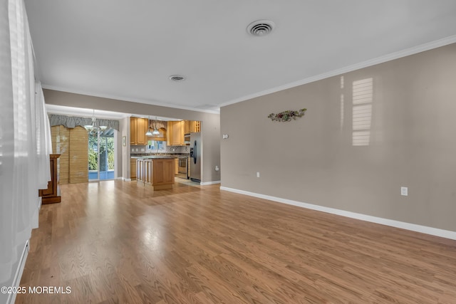 unfurnished living room featuring an inviting chandelier, ornamental molding, and light hardwood / wood-style flooring