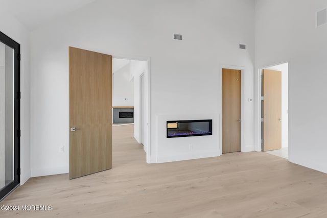 unfurnished living room featuring a towering ceiling and light hardwood / wood-style flooring