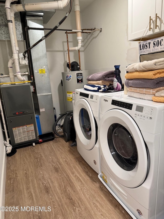 laundry area with water heater, cabinets, washing machine and clothes dryer, and light wood-type flooring