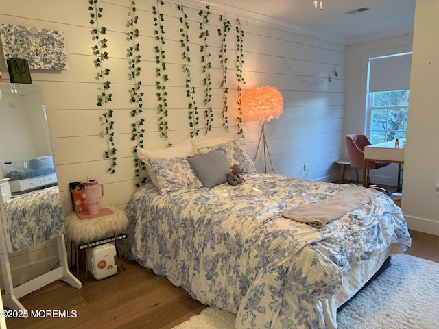 bedroom with hardwood / wood-style flooring, ornamental molding, and wood walls