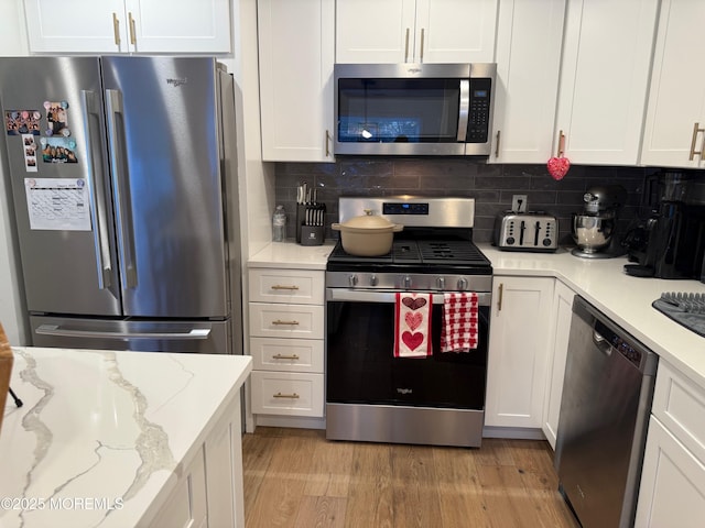 kitchen with stainless steel appliances, light stone countertops, light hardwood / wood-style floors, decorative backsplash, and white cabinets