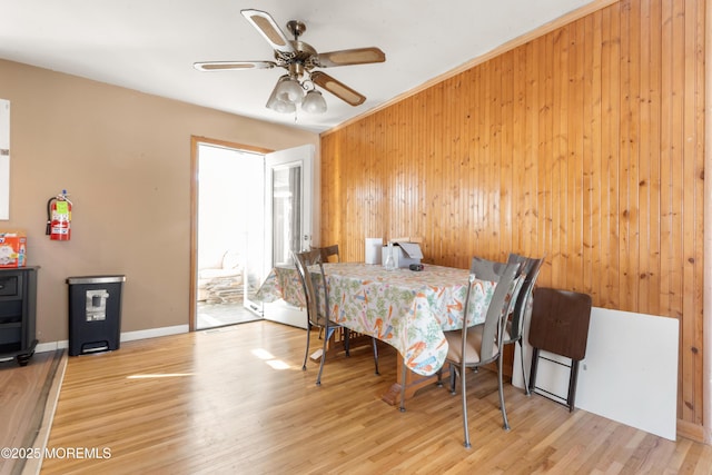 dining room featuring ceiling fan, light wood-type flooring, and wooden walls