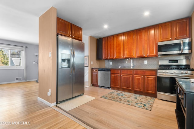 kitchen with tasteful backsplash, sink, light hardwood / wood-style flooring, and appliances with stainless steel finishes