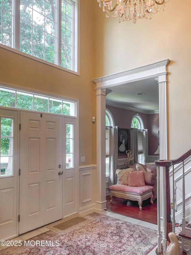 tiled entrance foyer featuring crown molding, a notable chandelier, a towering ceiling, and ornate columns