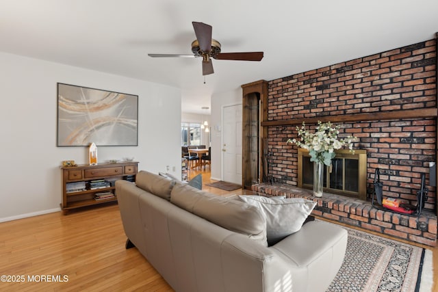 living room with a fireplace, ceiling fan, and light wood-type flooring