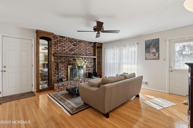 living room featuring a brick fireplace, ceiling fan, and light wood-type flooring