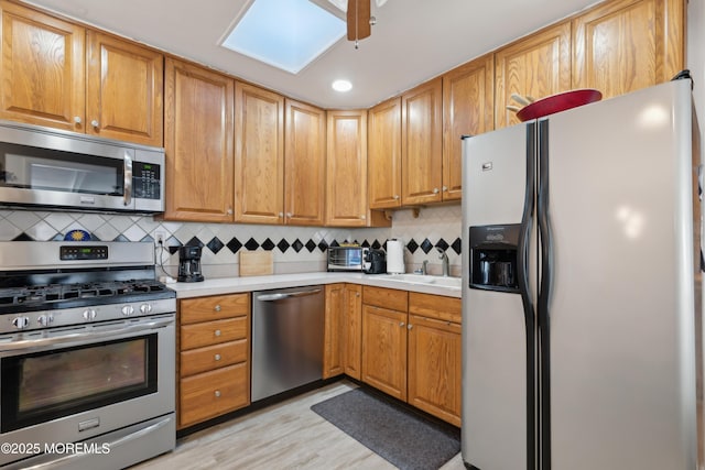 kitchen with sink, appliances with stainless steel finishes, a skylight, light hardwood / wood-style floors, and decorative backsplash