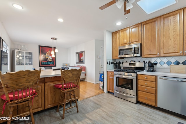 kitchen featuring backsplash, appliances with stainless steel finishes, hanging light fixtures, and light hardwood / wood-style flooring