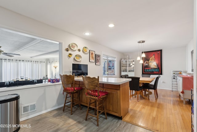 bar with hanging light fixtures, ceiling fan, and light hardwood / wood-style floors