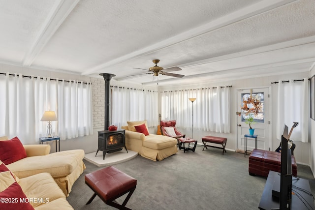 carpeted living room with ceiling fan, a wood stove, a textured ceiling, and beam ceiling