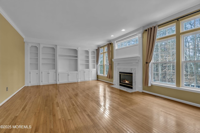 unfurnished living room featuring ornamental molding, a high end fireplace, built in features, and light wood-type flooring