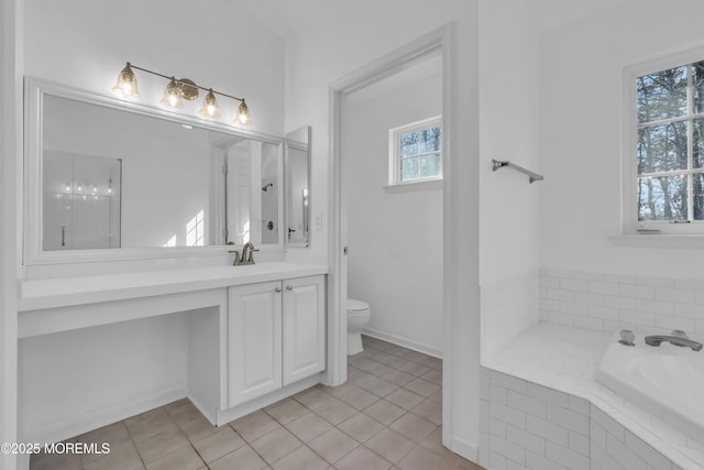 bathroom featuring tiled tub, vanity, tile patterned floors, and toilet