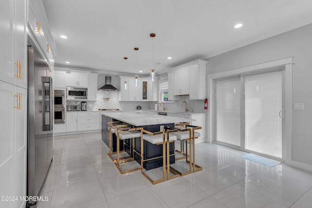 kitchen with white cabinetry, built in appliances, a kitchen breakfast bar, a kitchen island, and wall chimney range hood