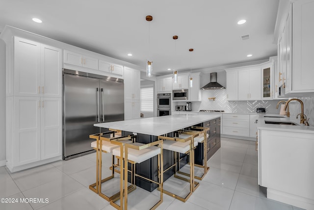 kitchen featuring built in appliances, a kitchen island, pendant lighting, wall chimney range hood, and white cabinets