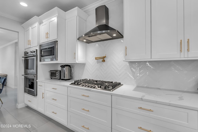 kitchen with wall chimney range hood, backsplash, stainless steel appliances, light stone countertops, and white cabinets