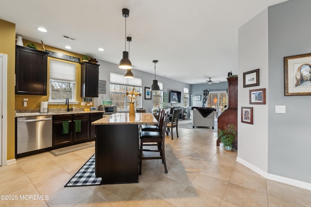 kitchen featuring pendant lighting, sink, light stone countertops, a kitchen island, and stainless steel dishwasher