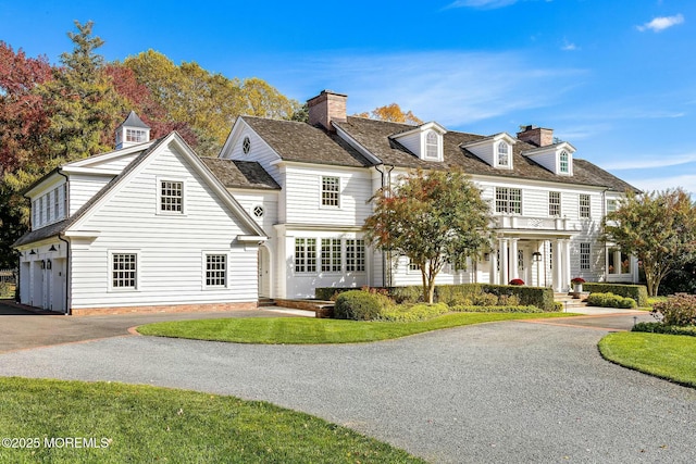 shingle-style home with aphalt driveway, a chimney, and a front lawn