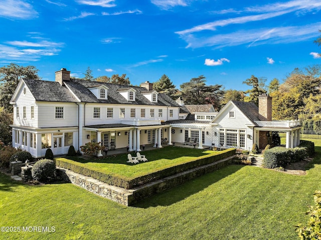 back of property with a patio area, a lawn, and a chimney