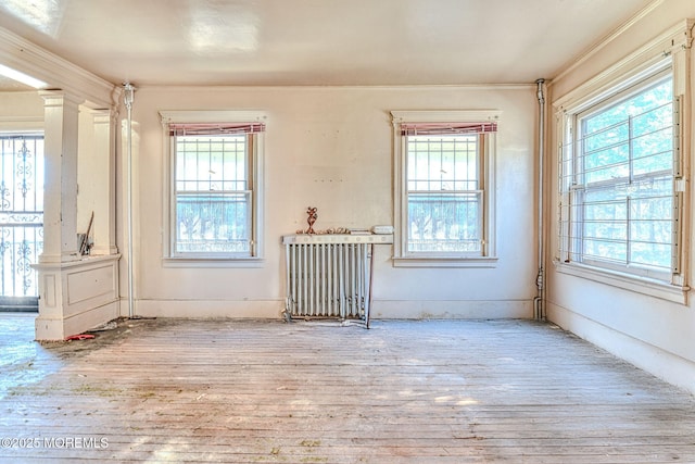 empty room with ornate columns, crown molding, plenty of natural light, and light hardwood / wood-style flooring