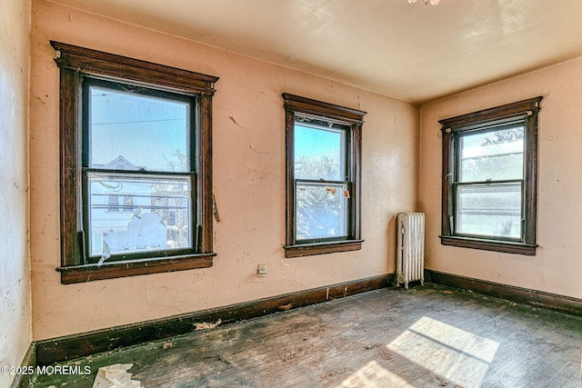 spare room with a healthy amount of sunlight, radiator heating unit, and dark hardwood / wood-style floors