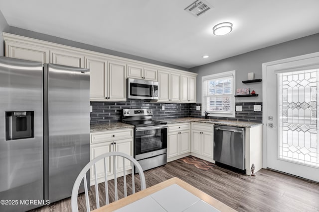 kitchen with wood-type flooring, sink, decorative backsplash, stainless steel appliances, and light stone countertops