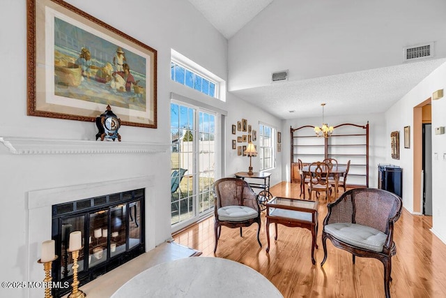 living area featuring vaulted ceiling, a textured ceiling, light hardwood / wood-style flooring, and a notable chandelier