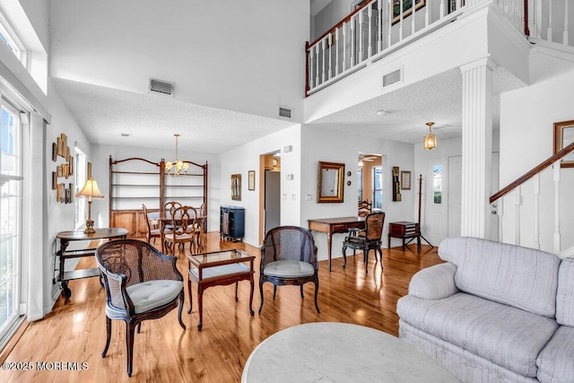 living room with light hardwood / wood-style flooring, an inviting chandelier, decorative columns, a high ceiling, and a textured ceiling