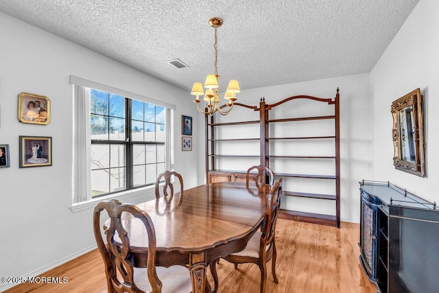 dining space with a notable chandelier, a textured ceiling, and light wood-type flooring