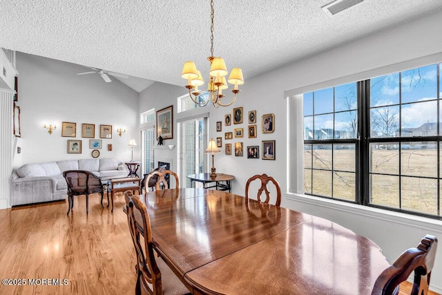 dining room with lofted ceiling, ceiling fan with notable chandelier, light hardwood / wood-style flooring, and a textured ceiling