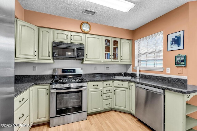 kitchen featuring appliances with stainless steel finishes, sink, backsplash, green cabinets, and light hardwood / wood-style floors