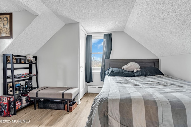 bedroom with lofted ceiling, a baseboard heating unit, light hardwood / wood-style flooring, and a textured ceiling