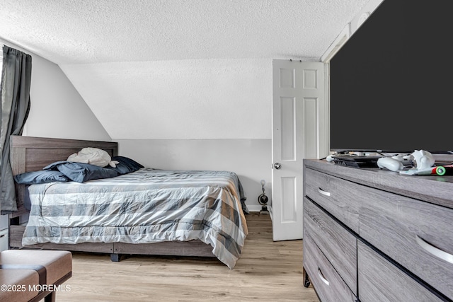 bedroom with lofted ceiling, light hardwood / wood-style flooring, and a textured ceiling