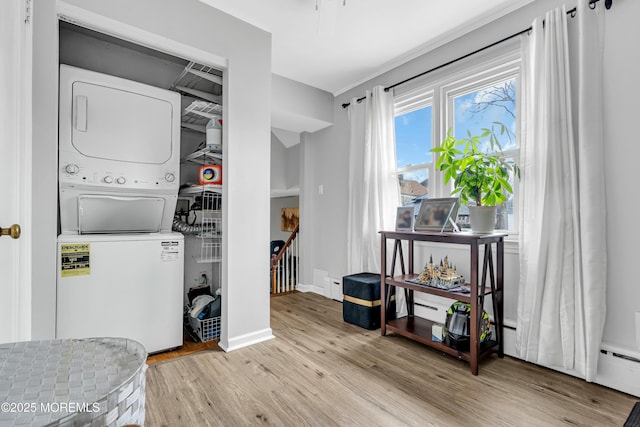 clothes washing area with stacked washing maching and dryer, a baseboard heating unit, and light hardwood / wood-style flooring