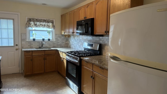 kitchen featuring stainless steel gas stove, sink, decorative backsplash, white refrigerator, and light stone counters